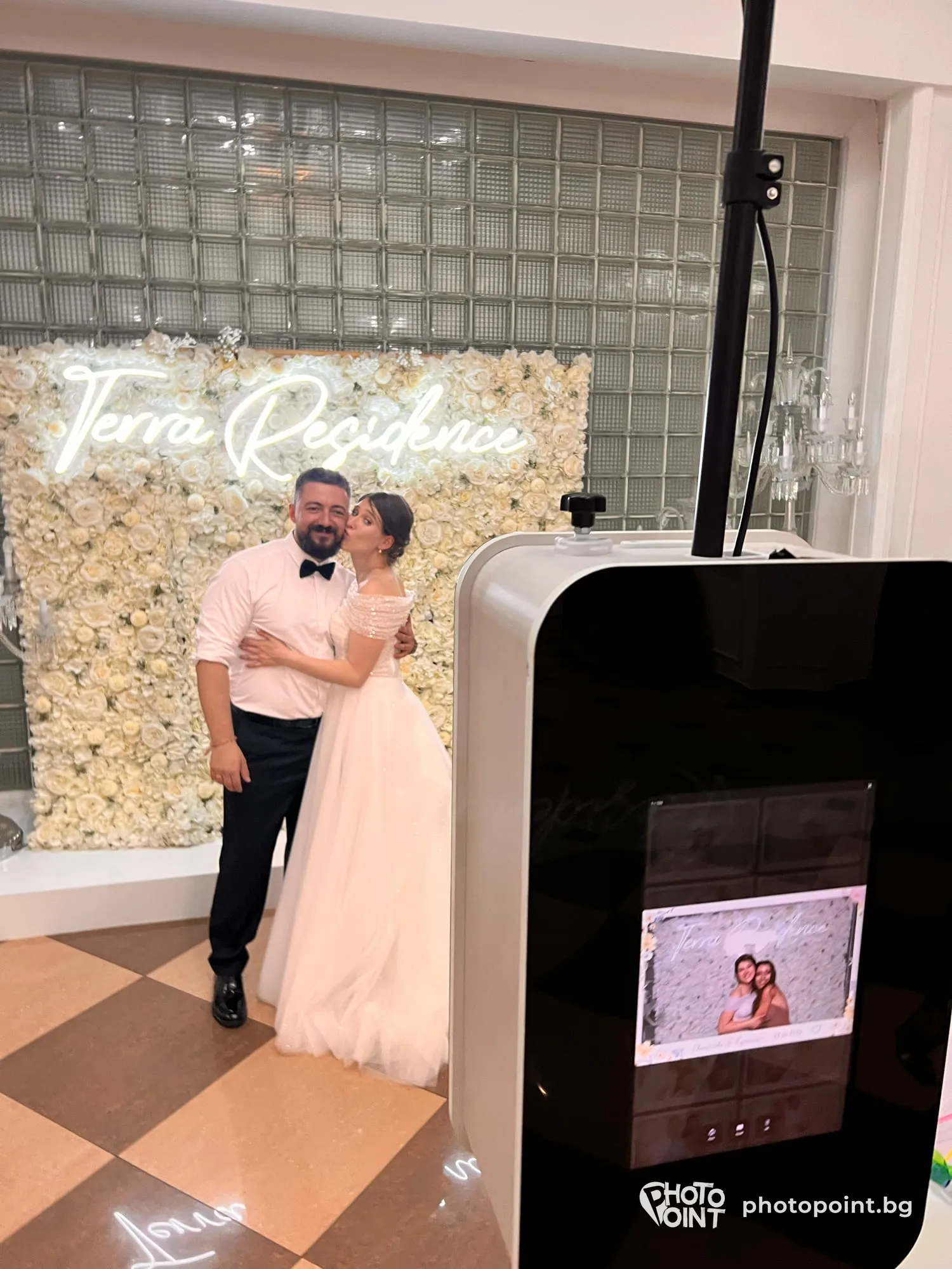 A bride and groom at a flower wall, with PremiumPoint beside them
